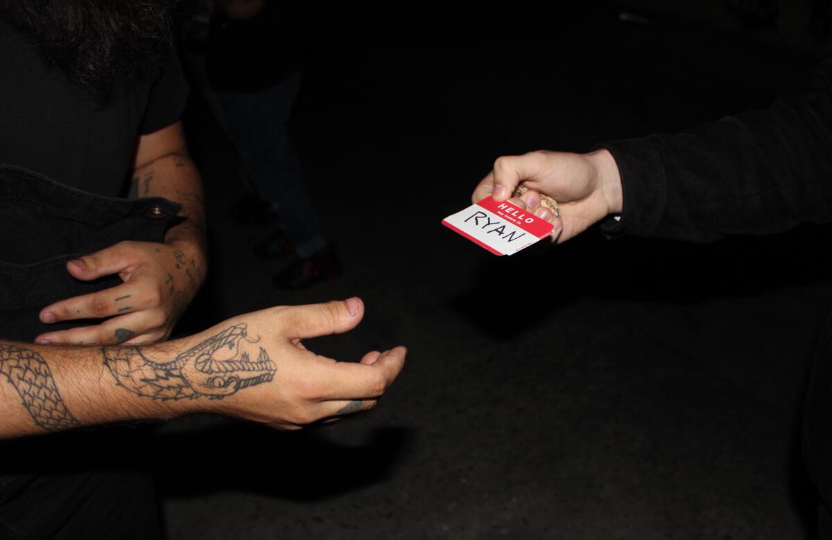 A hand reaches out toward another person holding a name tag with the word Ryan 