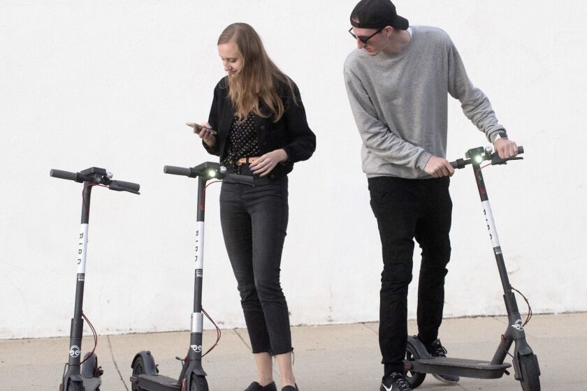 Altadena, CA - January 18, 2019 - Kylee Kramer, left, and Adam Baker, right, both of Altadena, use an app to pay and unlock Bird Scooters near Lake Avenue in Altadena. (Ana Venegas / For The Times)