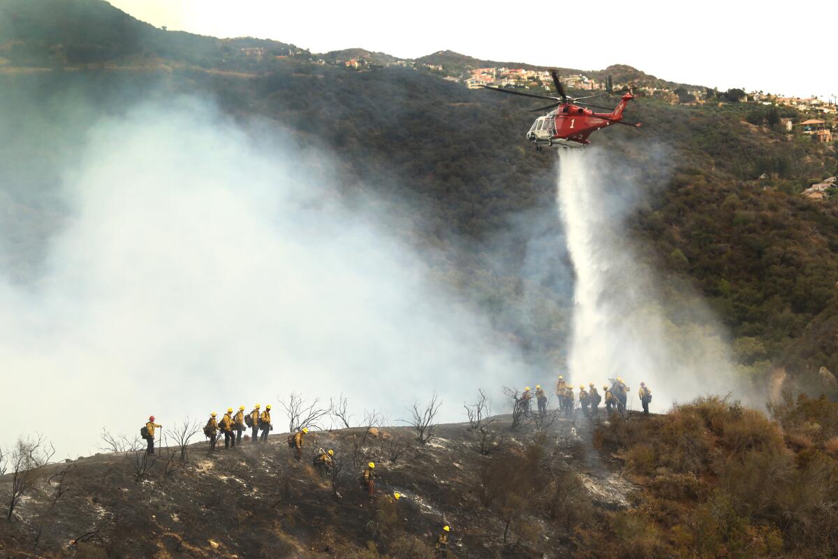 Firefighters and a water-dropping helicopter work the fire line between Pacific Palisades and Topanga Canyon on May 16.
