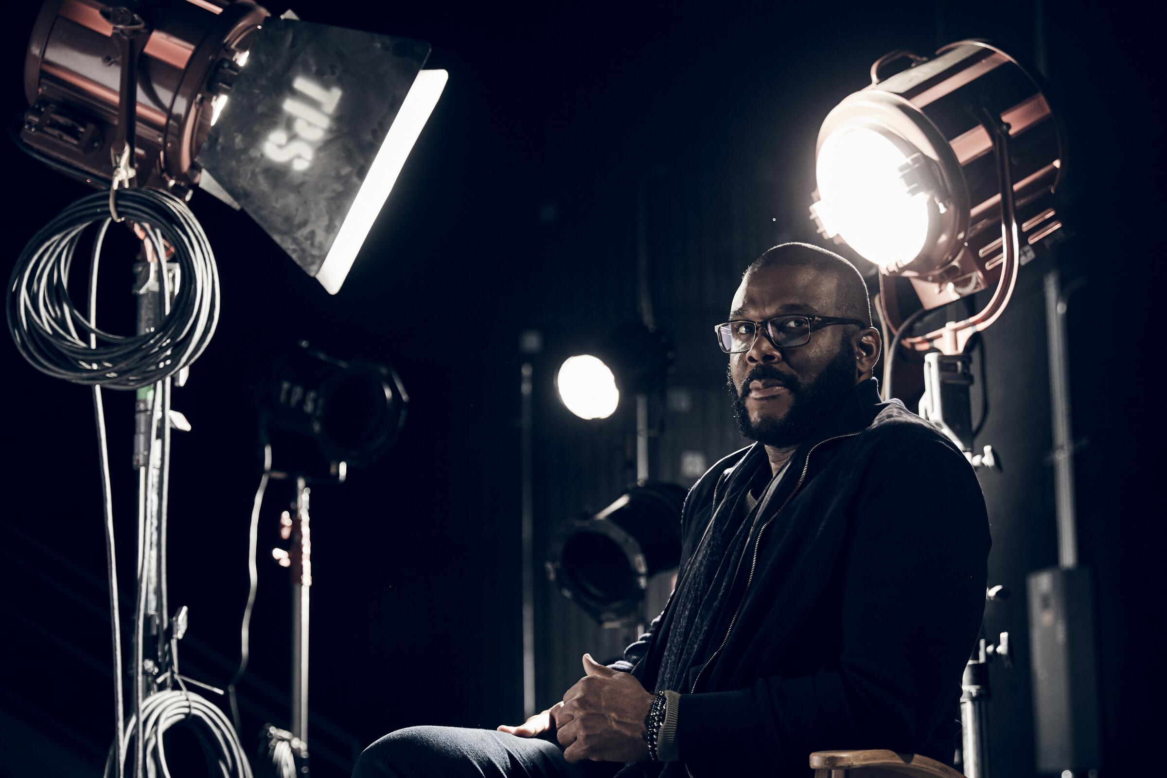 A man seated amid bright movie lights.