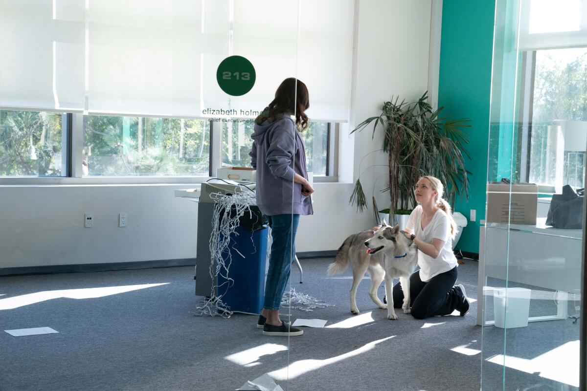 A woman plays with a dog while another woman looks on in a scene from "The Dropout."