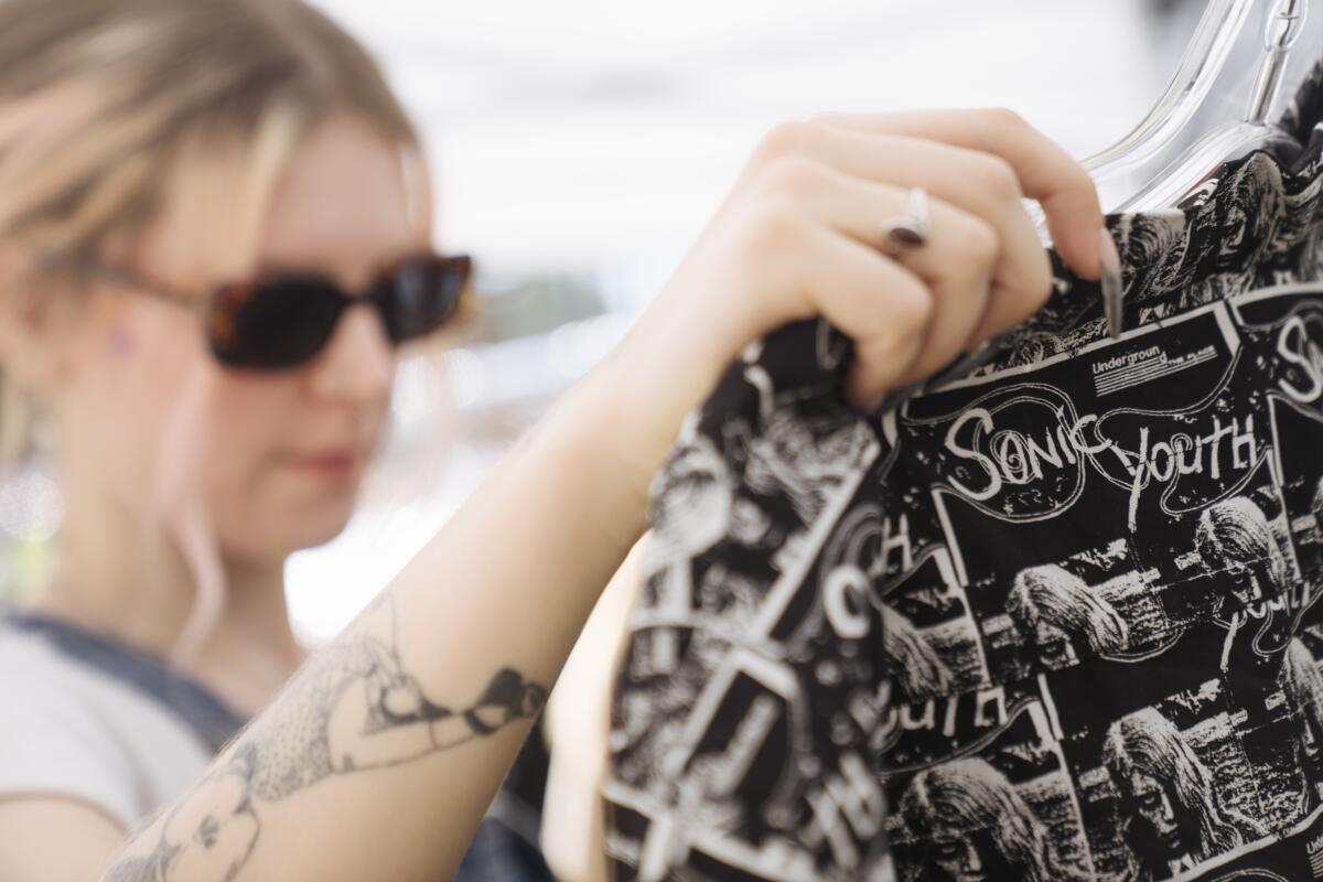 A woman in sunglasses holds up a shirt with the words "Sonic Youth" as part of a black-and-white design