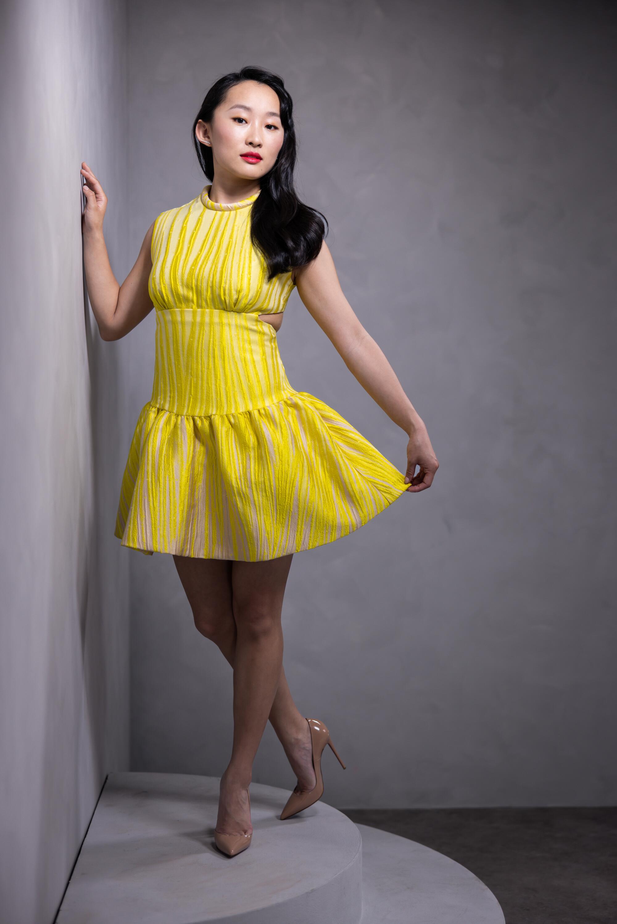  Wearing a bright yellow dress, Ji-young Yoo leans against a wall for a portrait.