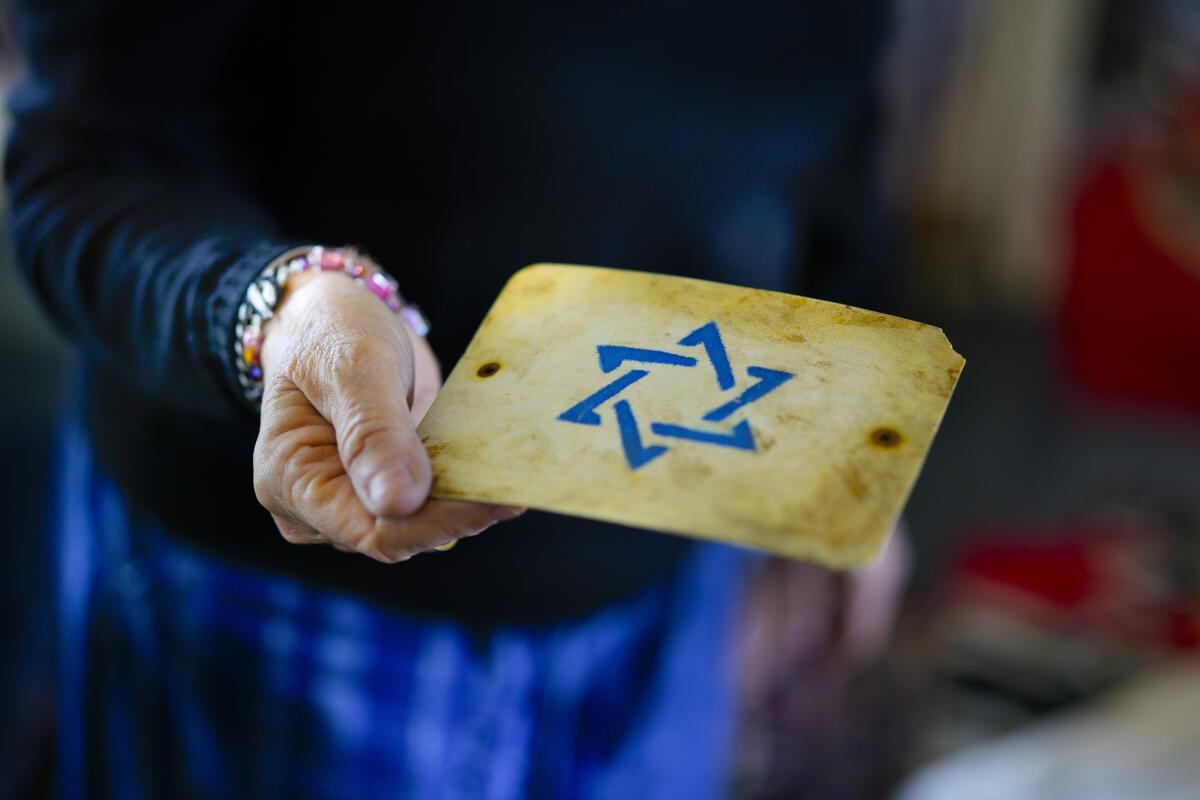 A woman holds a small, weathered plaque bearing a blue star of David.