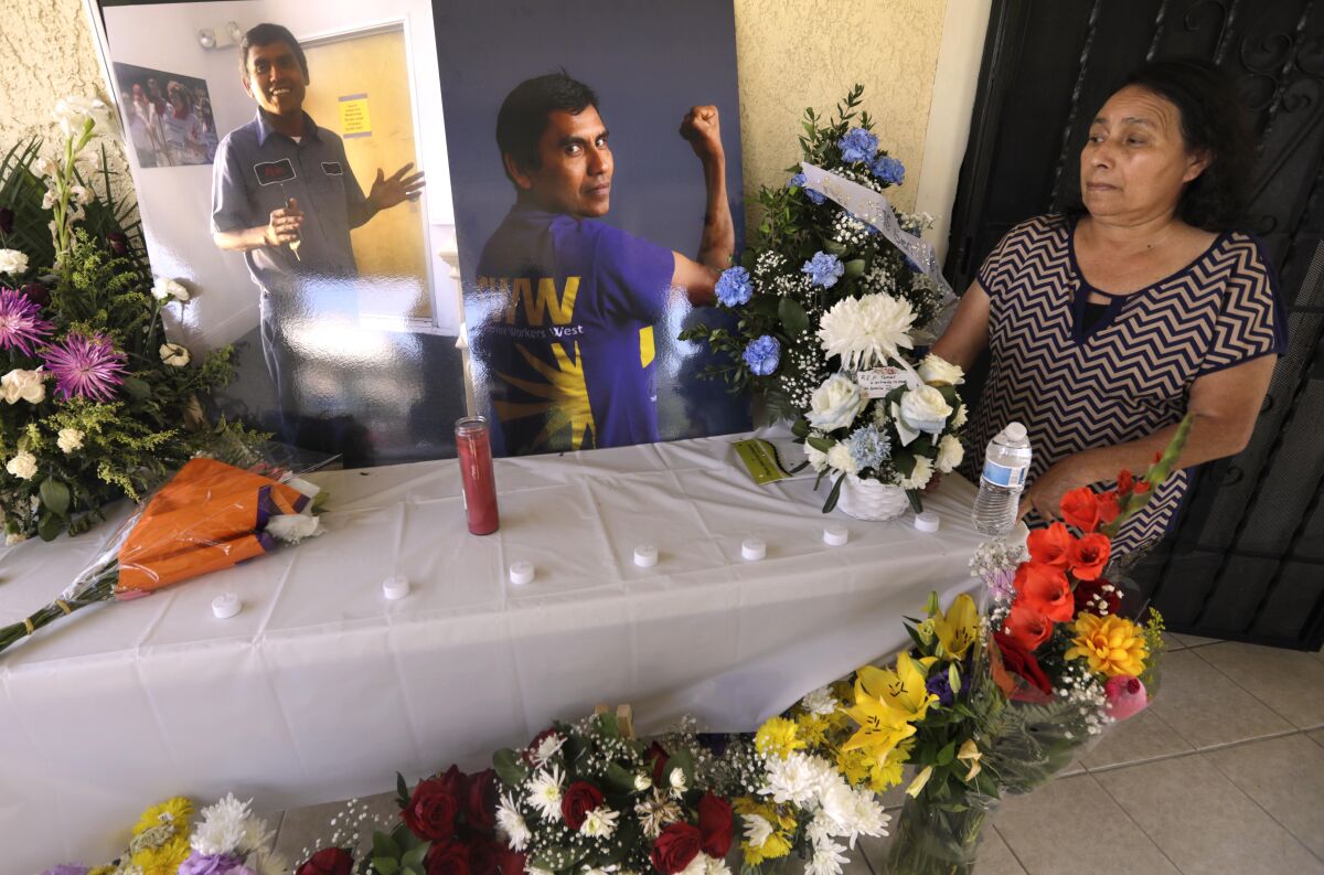 A woman stands alongside a table with candles and flowers and photos of a man.