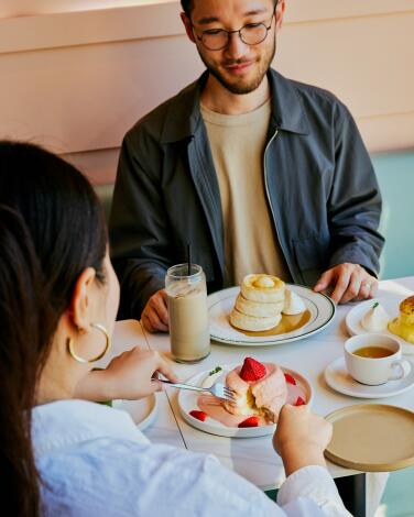 A man and a woman at a restaurant table with piles of tall fluffy pancakes