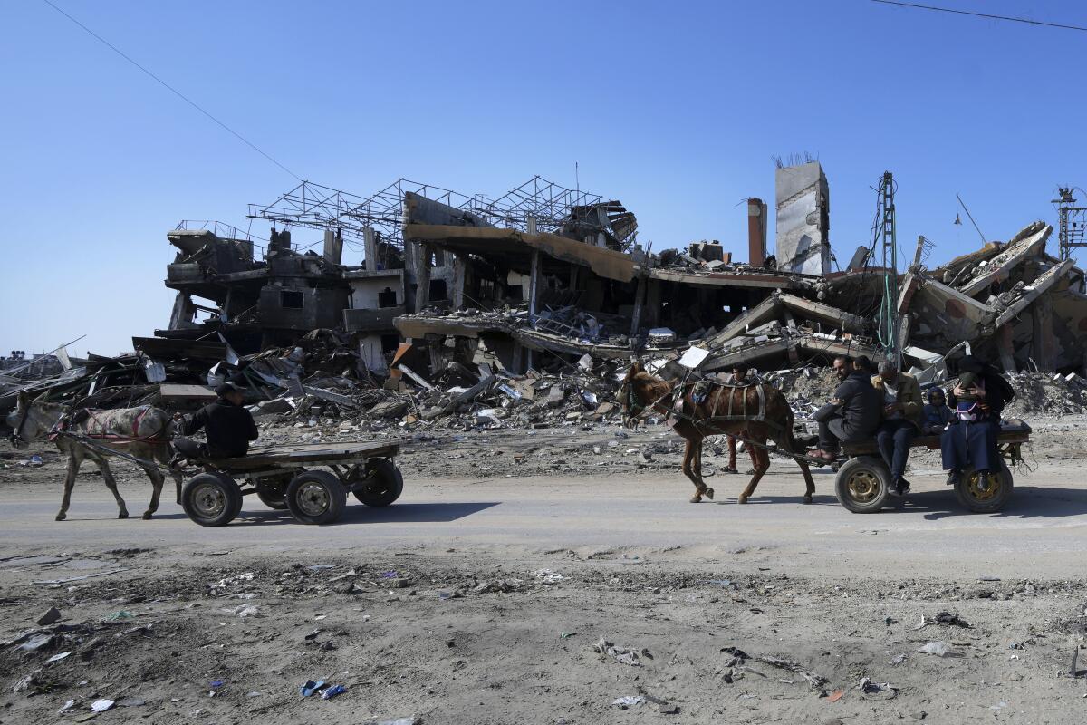 Palestinos pasan en carros tirados por burros junto a la destruccin causada por los bombardeos israeles en la carretera de Salah el Dein, en el campo de refugiados de Maghazi, en el centro de la Franja de Gaza, el 16 de febrero de 2024. (AP Foto/Adel Hana)