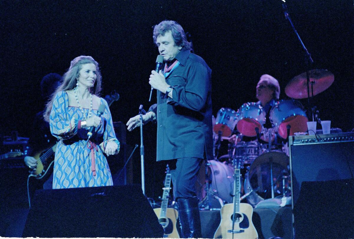 A man and woman singing on stage with a drummer behind them