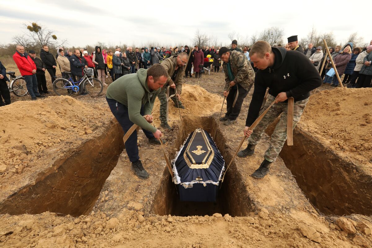 Men lower a coffin into a grave as a crowd looks on 