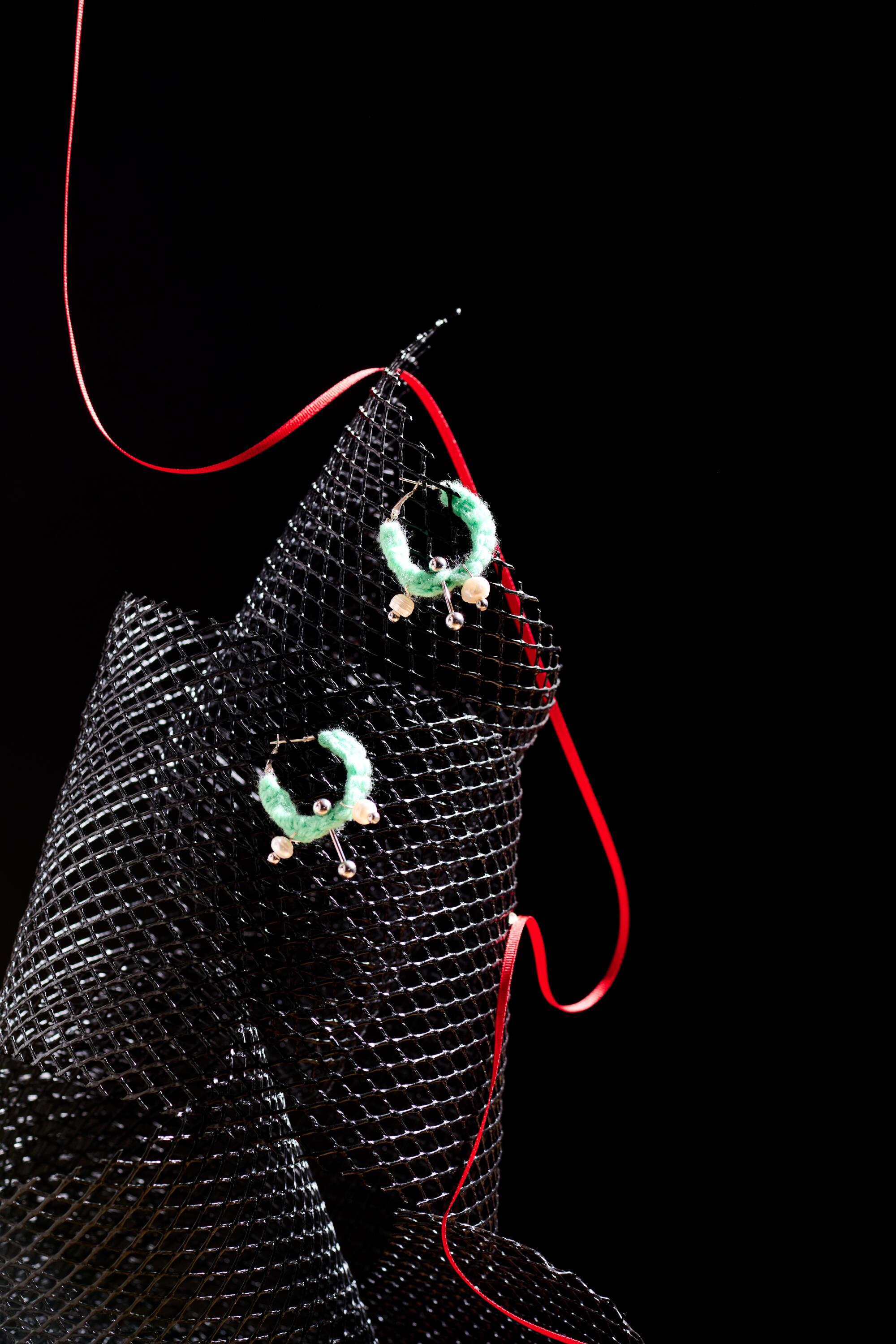 Green hoop earrings on black material near a red plastic string.