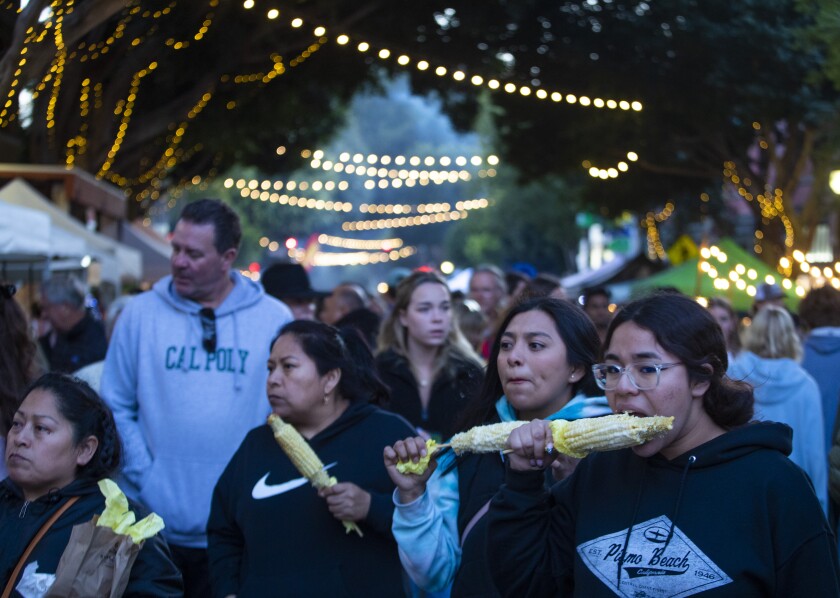 People eat corn on the cob at dusk in an open-air market.