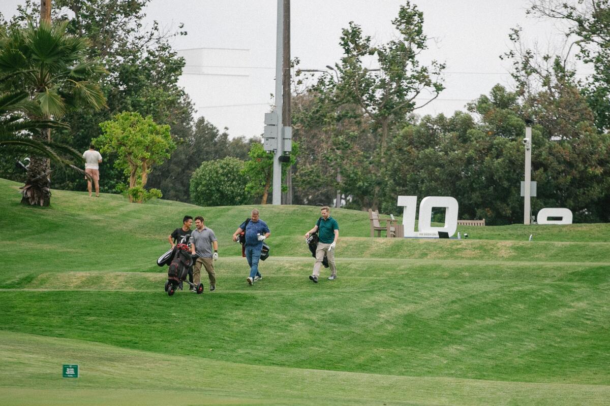 Golfers walk on rolling terrain