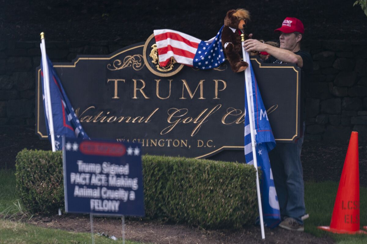 A supporter of President Trump places a "Trumpy Bear" atop the sign of Trump National Golf Club.