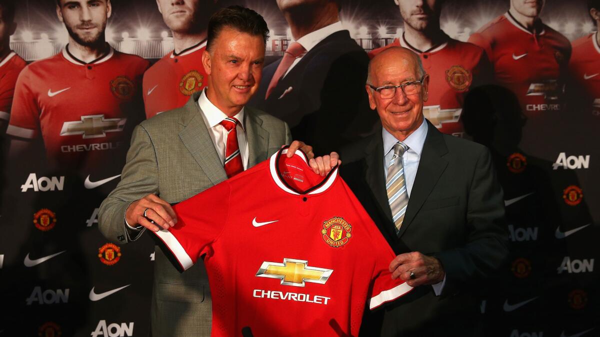 Louis van Gaal, left, holds up a Manchester United jersey with soccer great Bobby Charlton while being introduced as the team's new coach Thursday. Chevrolet has paid more than half a billion dollars to have its logo featured prominently on Manchester United's jerseys.
