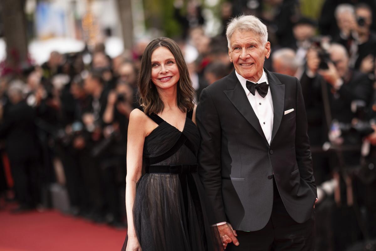Calista Flockhart and Harrison Ford hold hands and walk a red carpet in formalwear