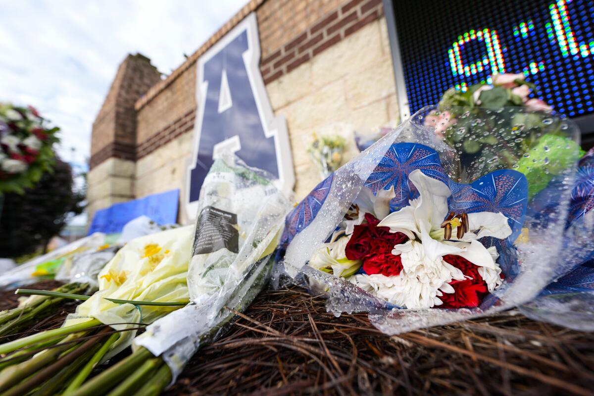 Flowers are piled on a makeshift memorial by a wall. 