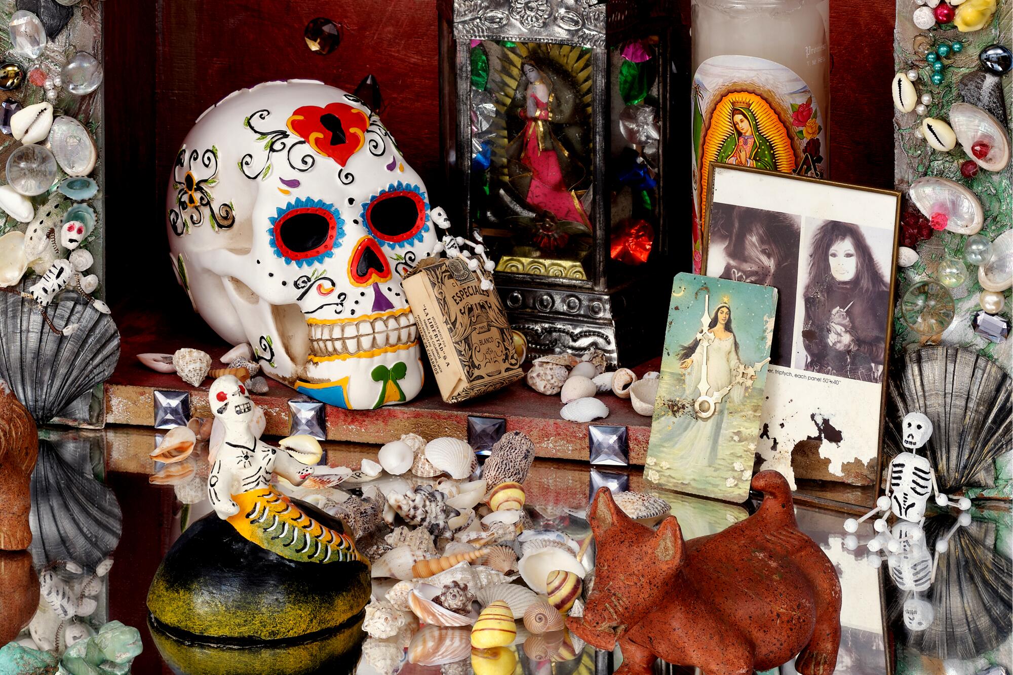 A detail of an altar shows a painted plaster skull, a pre-Columbian-style ceramic, candles, photos and seashells