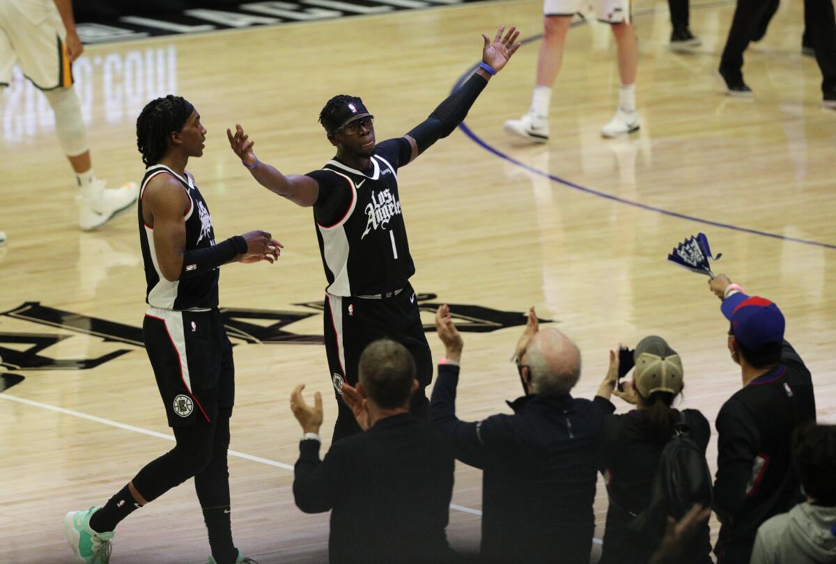 Reggie Jackson, alongside Terance Mann, lifts up both arms in front of applauding fans.