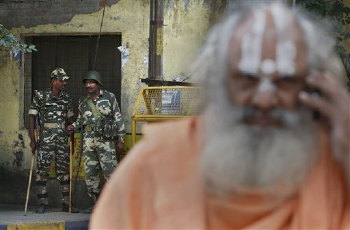 Indian paramilitary soldiers stand guard as a Hindu holy man talks on a mobile phone outside the Lucknow High Court in Lucknow, India, Thursday, Sept. 30, 2010. An Indian court ruled Thursday that a disputed holy site that has sparked bloody communal riots across the country in the past should be divided between the Hindu and Muslim communities. However, the court gave the Hindu community control over the section where the now demolished Babri Mosque stood and where a small makeshift tent-shrine to the Hindu god Rama rests. While both Muslim and Hindu lawyers vowed to appeal to the Supreme Court, the compromise ruling seemed unlikely to set off a new round of violence, as the government had feared. (AP Photo/Mustafa Quraishi)