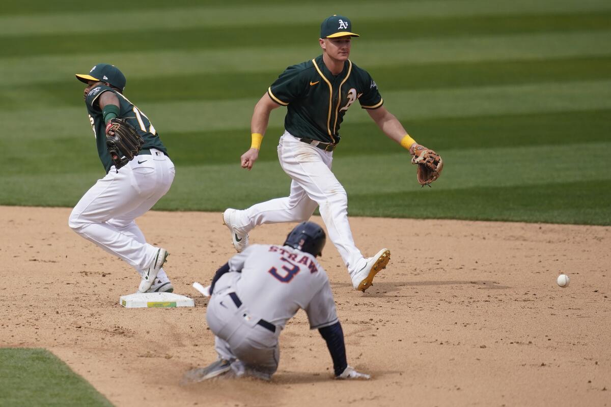 Oakland Athletics shortstop Elvis Andrus, left, cannot field a throwing error by third baseman Matt Chapman, top, as Houston Astros' Myles Straw (3) advances to second base during the sixth inning of a baseball game in Oakland, Calif., Sunday, April 4, 2021. (AP Photo/Jeff Chiu)