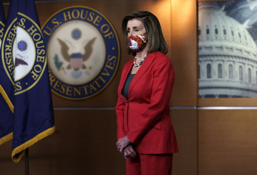 House Speaker Nancy Pelosi stands with her arms crossed wearing a mask in a room at the Capitol