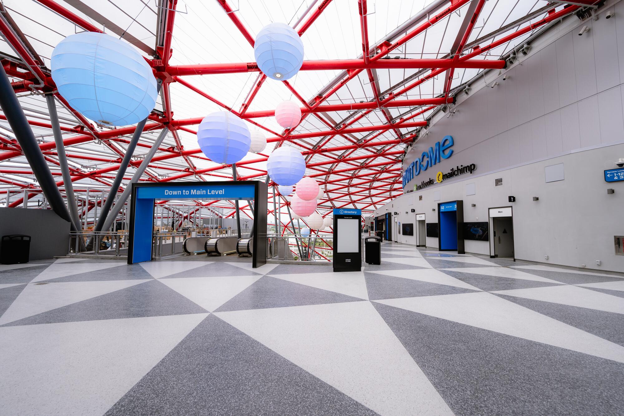 Exposed structural steel creates a pattern of red triangles over a concourse inside Intuit Dome. 