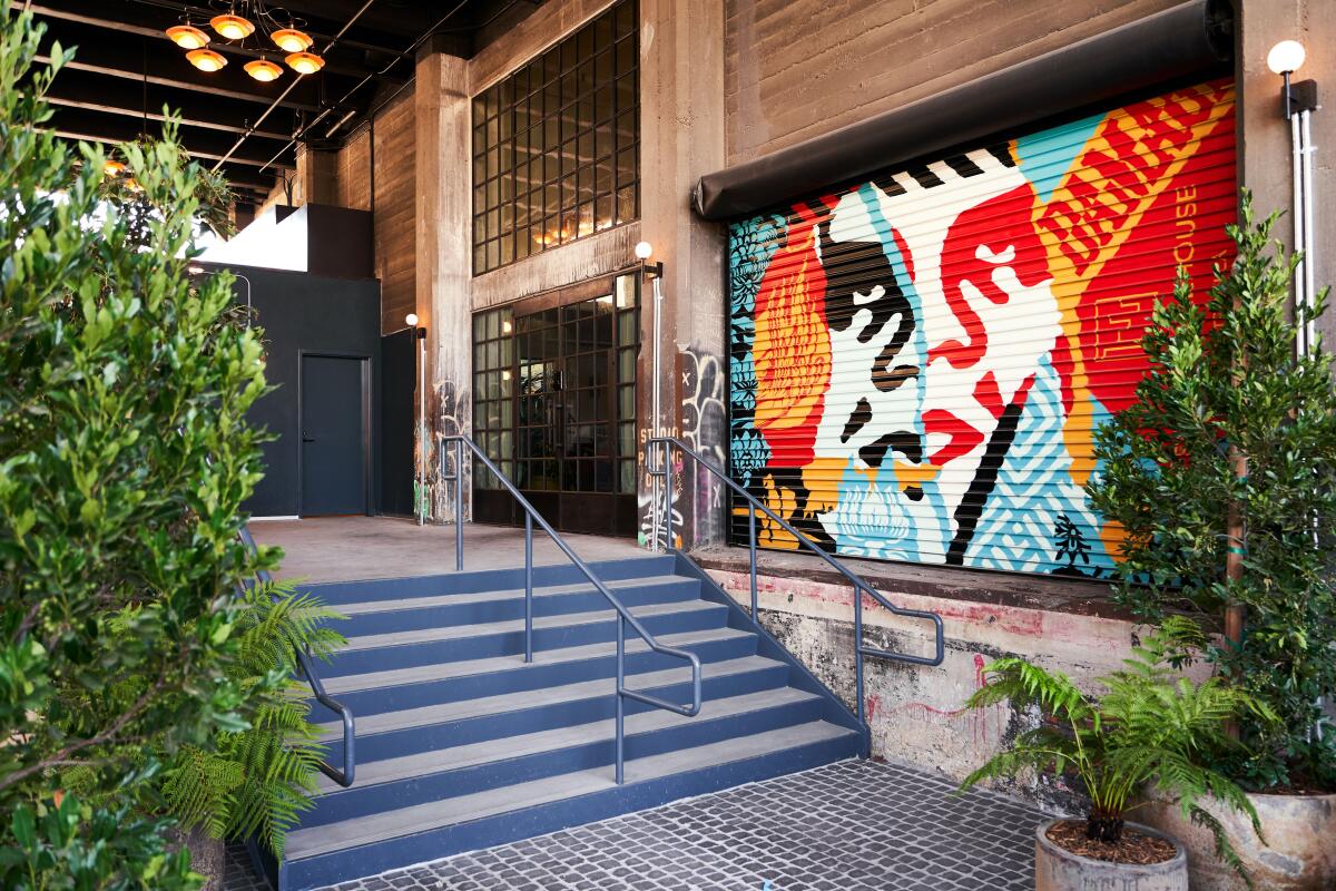 The steps leading to a building entrance pass a colorful mural and shrubbery.