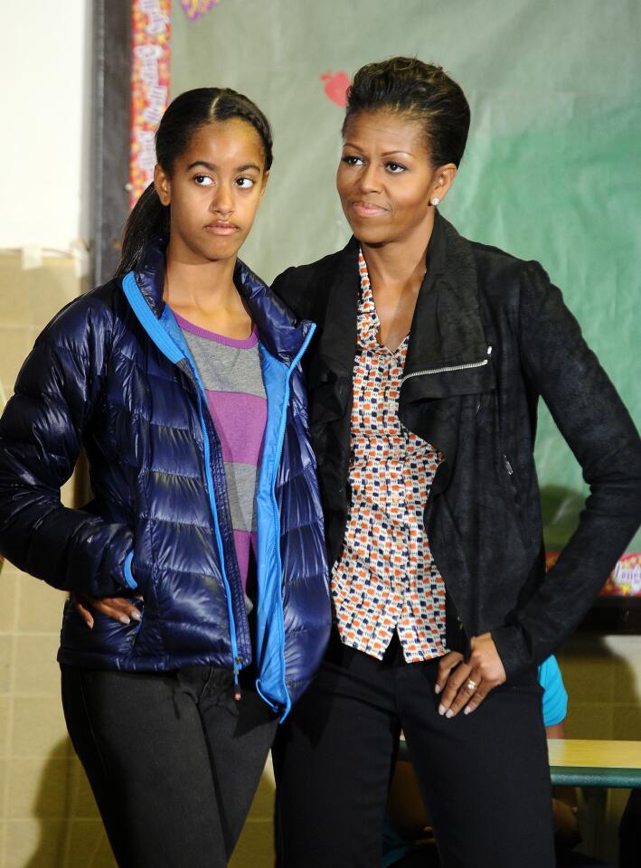 First Lady Michelle Obama, in a casual print top, textured leather jacket and dark jeans, and daughter Malia listen as President Obama speaks to volunteers at the Browne Education Center in Washington in January of 2012.