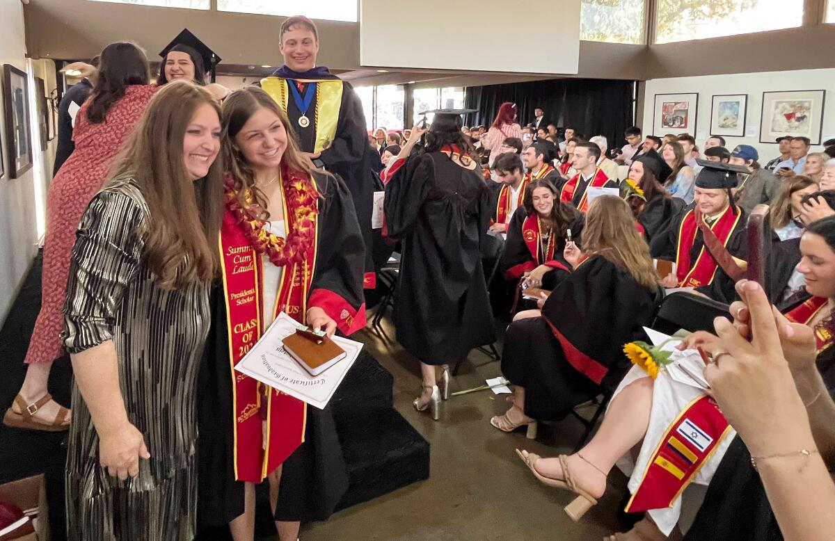 A smiling graduate stands for a photo among others clad in gowns with USC's cardinal and gold colors