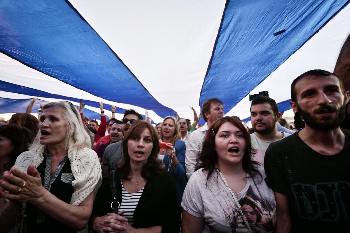 Greeks in favor of remaining in the Eurozone demonstrate in front of the parliament in Athens, singing the national anthem as they carry a giant Greek flag.