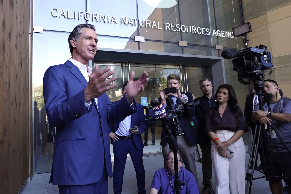 Gov. Gavin Newsom gestures while speaking in front of reporters, microphones and TV cameras.