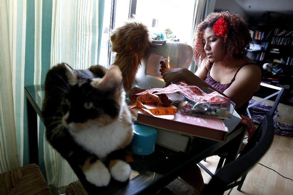 Jonaya Kemper, a member of the millennial generation, makes a scarf for a friend in Los Angeles' Thai Town while her cat chills out nearby. A new Pew surveys says millennials are more upbeat than others about their finances and the nation's future but are cool to many traditions, such as political parties and religious affiliations.