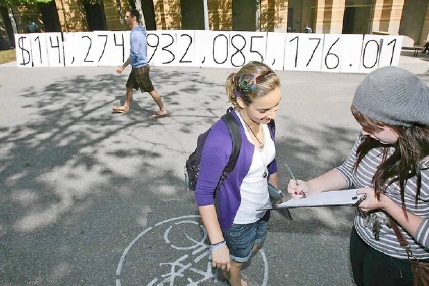 Amanda Flack, 20, right, and Amanda Minsky, 18, sign a petition in front of a "National Debt Clock" set up by Young Americans for Liberty at UC Irvine on Tuesday. The number stands at more than $14 trillion.