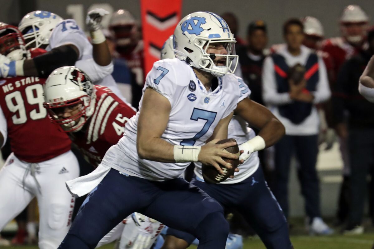 FILE - North Carolina quarterback Sam Howell (7) rolls out while being chased by North Carolina State defensive tackle Davin Vann (45) during the first half of an NCAA college football game Friday, Nov. 26, 2021, in Raleigh, N.C. The junior quarterback started his career at North Carolina in 2019 by leading the Tar Heels to a win over South Carolina at Bank of America Stadium in the season opener. Now the projected first round NFL draft pick will look to close out his career with a victory over Gamecocks at the same stadium in the Duke's Mayo Bowl. (AP Photo/Chris Seward, File)