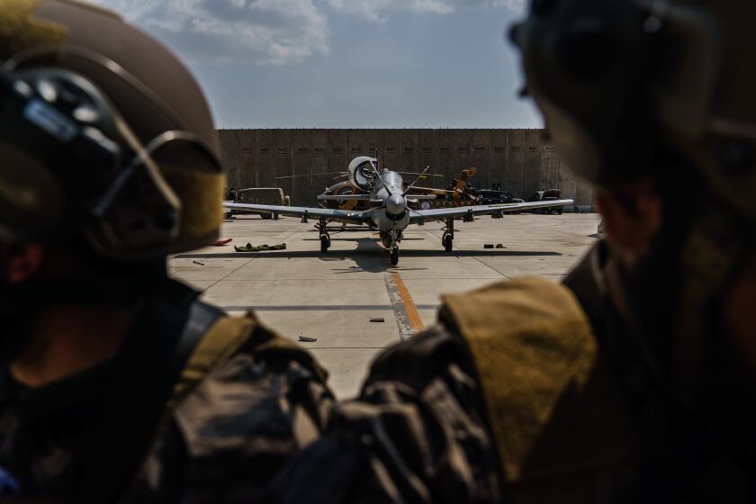 KABUL, AFGHANISTAN -- AUGUST 31, 2021: Taliban fighters stand ready in front of the Afghan A-29 Super Tucano, as the militant group secure the Hamid Karzai International Airport, in the wake of the American forces completing their withdrawal from the country in Kabul, Afghanistan, Tuesday, Aug. 31, 2021. (MARCUS YAM / LOS ANGELES TIMES)