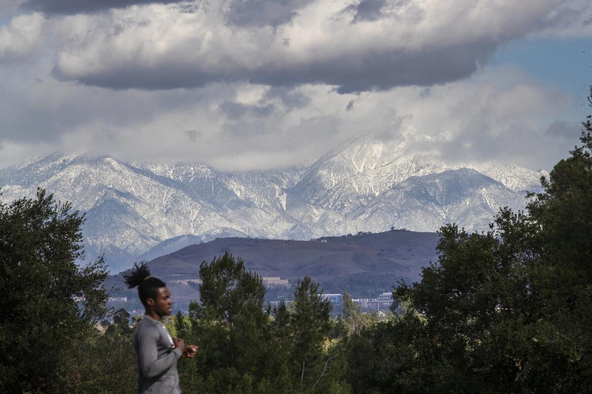 A runner has a little help from gusty winds while exercising with a view of snow-capped San Gabriel Mountains.