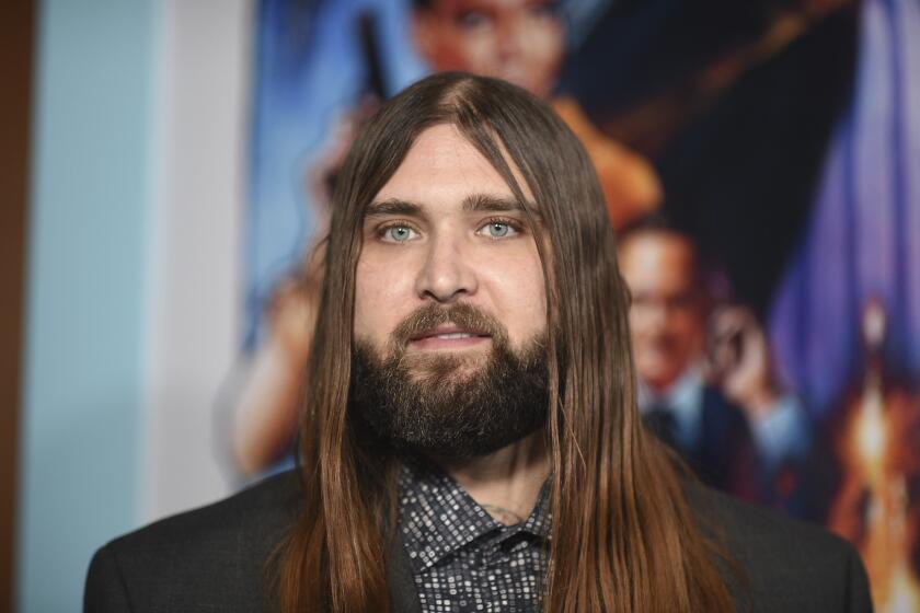 Weston Cage, who has long brown hair and a beard, poses at a movie premiere in a spotted shirt and black blazer