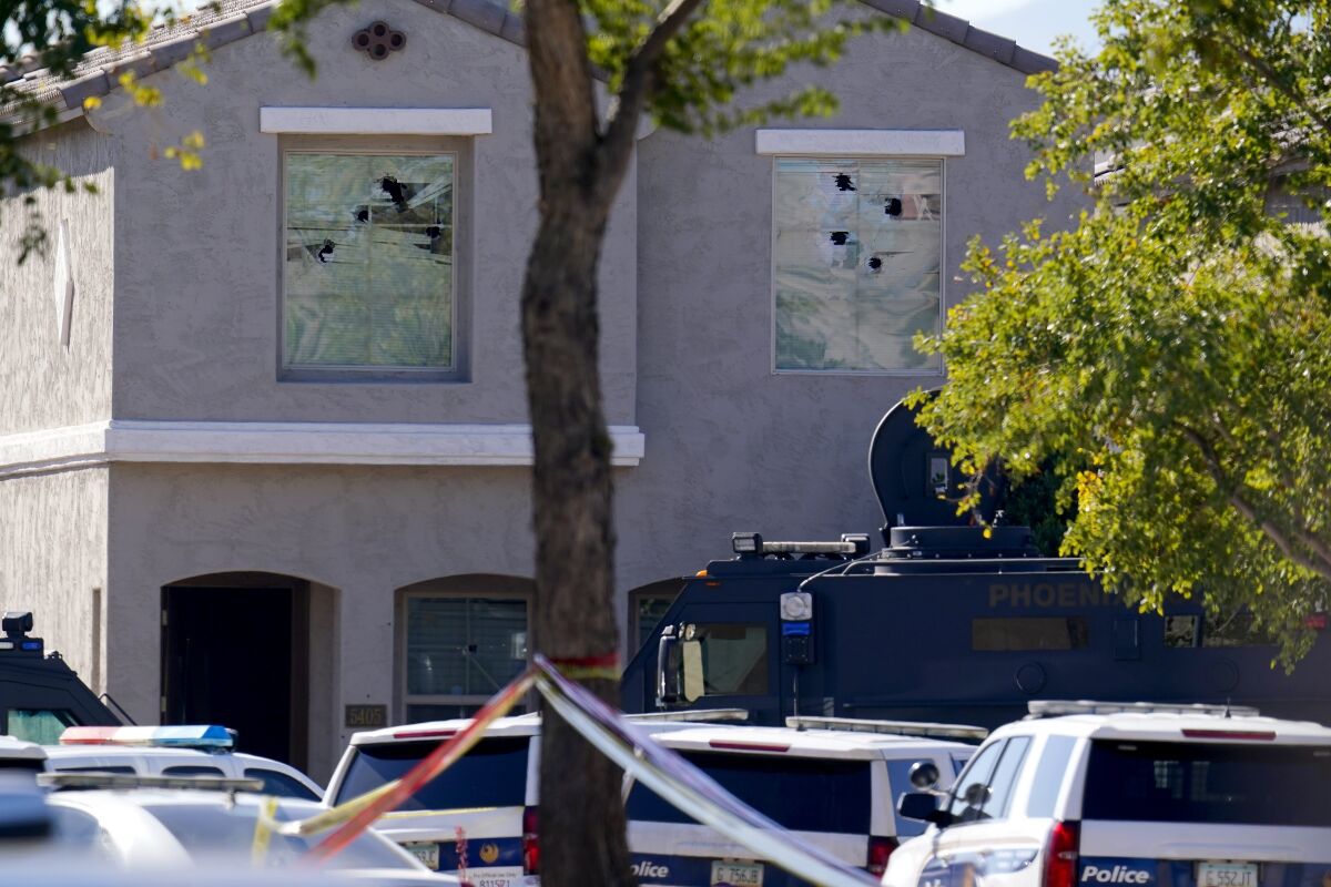 Multiple holes in windows can be seen at a house where four Phoenix Police Department officers were shot and four others were injured after responding to a shooting inside the home Friday, Feb. 11, 2022, in Phoenix. The shooting suspect was found dead in the home following a barricade situation, and a woman at the home was critically injured. (AP Photo/Ross D. Franklin)