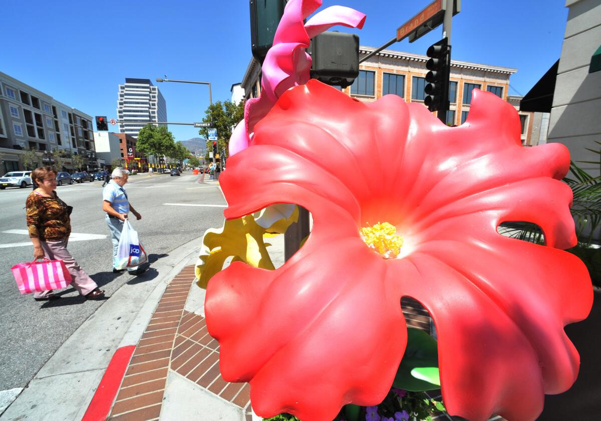 Pedestrians walk by a giant flower pot filled with oversized, artificial flowers across from the Americana at Brand on Thursday, April 9, 2015.