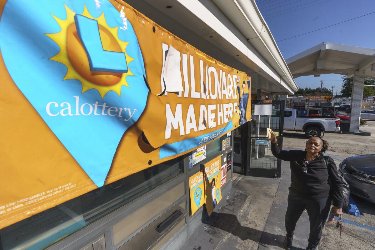 A woman holds up a lottery ticket while standing near a California Lottery banner outside Joe's Service Center in Altadena.