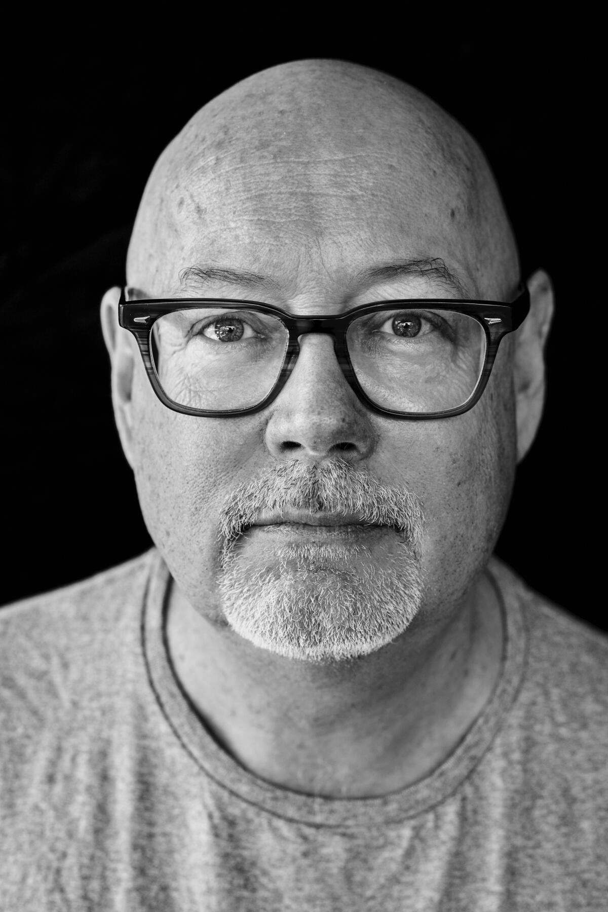 A black-and-white headshot of a man with thick-rimmed glasses 