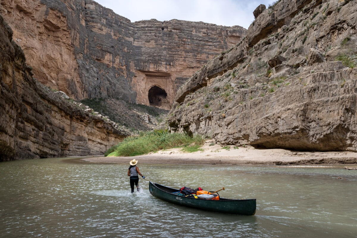 A person pulls a canoe along a shallow river in a canyon 