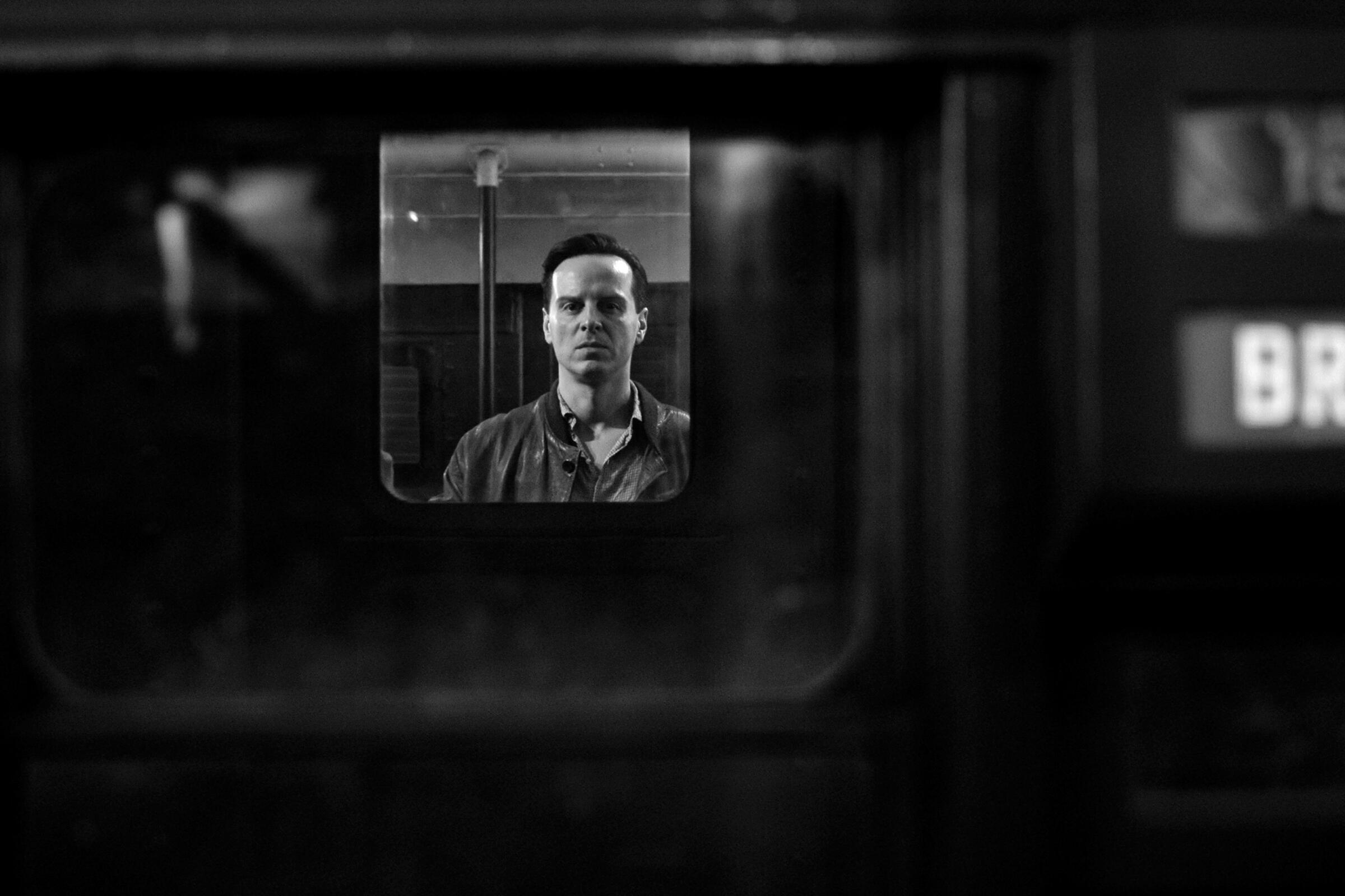In a black-and-white image, a man stands inside a train looking out the window in "Ripley."