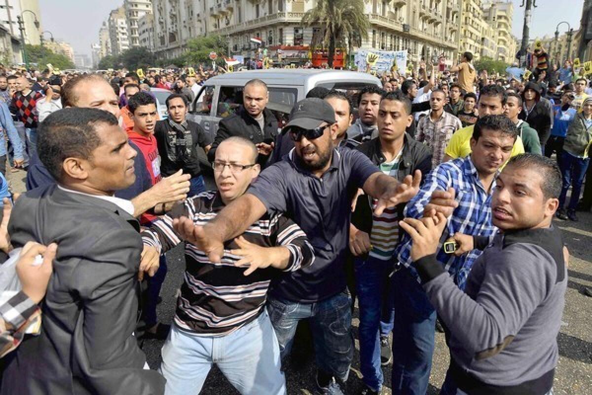 An Egyptian intervenes as government supporters, left, clash with backers of deposed Islamist President Mohamed Morsi in Cairo, where Morsi's trial got underway.