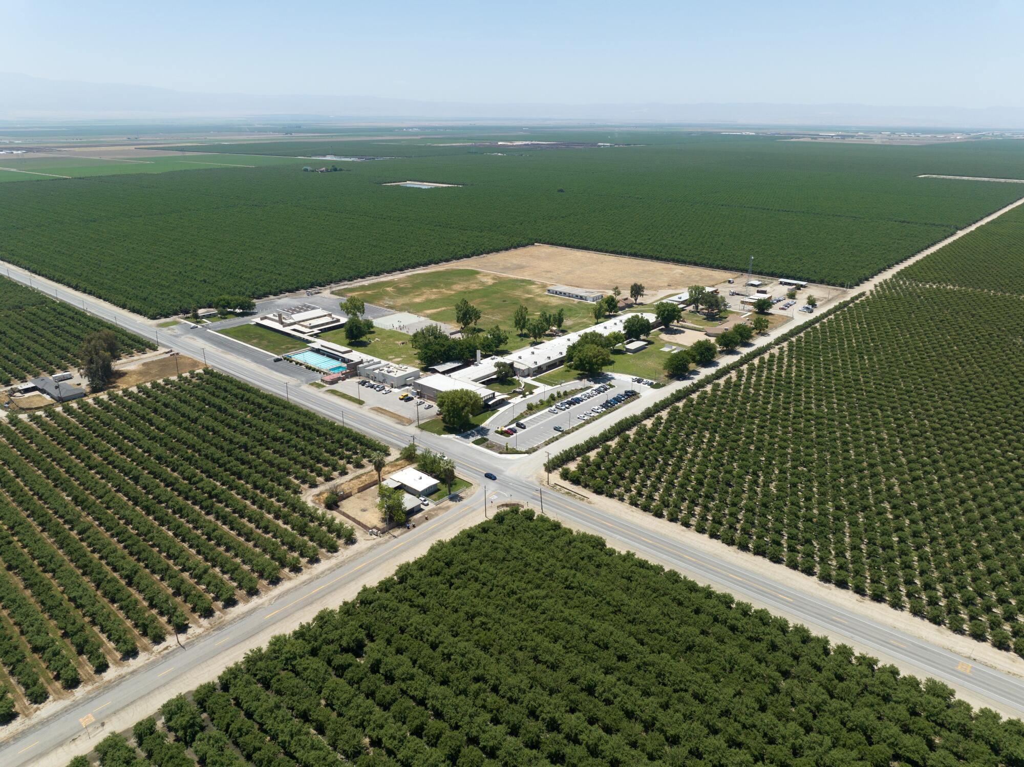 An aerial photograph shows a school campus surrounded by orchards.