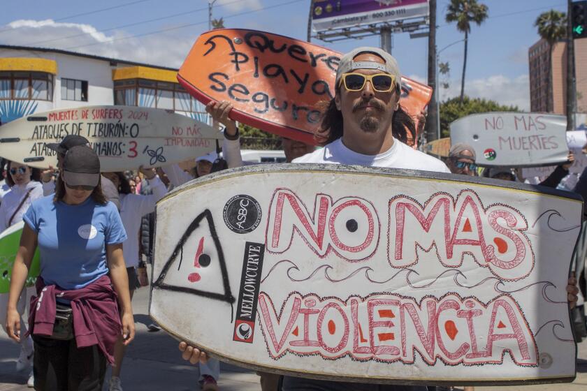 A demonstrator holding a bodyboard written in Spanish " No more violence" protests the disappearance of foreign surfers in Ensenada, Mexico, Sunday, May 5, 2024. Mexican authorities said Friday that three bodies were recovered in an area of Baja California near where two Australians and an American went missing last weekend during an apparent camping and surfing trip. (AP Photo/Karen Castaneda)