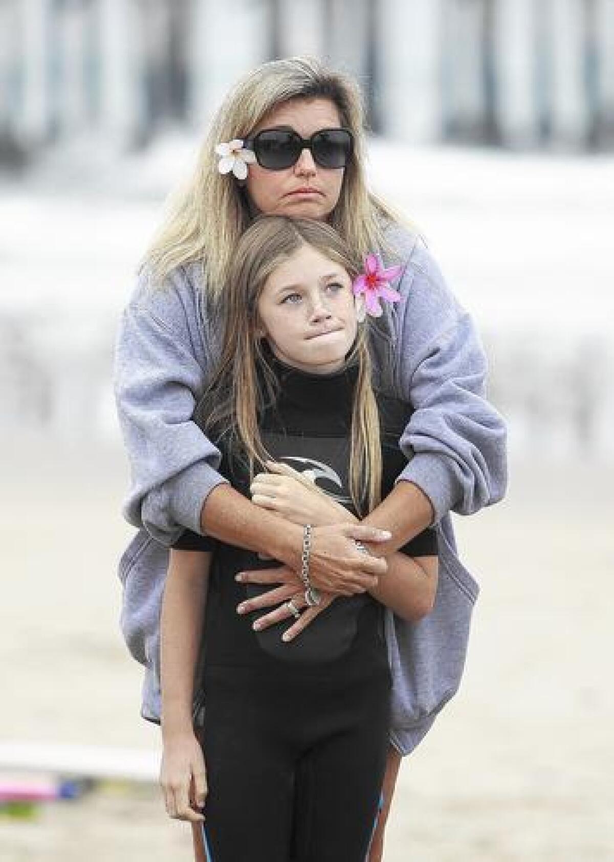 Kori Johnson and her daughter Kyra, 10, look on as friends and family prepare to participate in her husband Kyle's memorial paddleout at the Newport Pier on Saturday. Kyle Johnson was involved in an automobile accident near the Arizona-California border on Father's Day, and died early the next morning. He was 42.