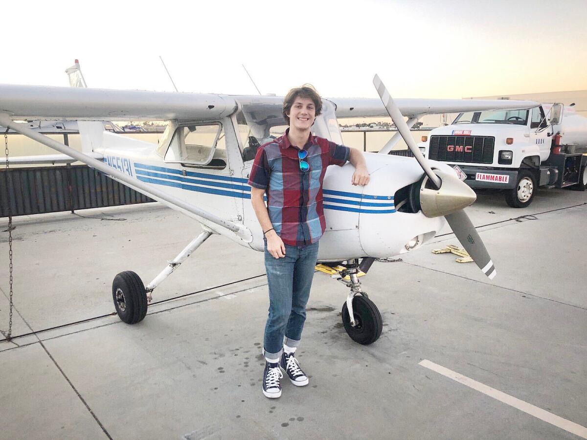 A young man poses for a photo while leaning against a small single-propeller plane