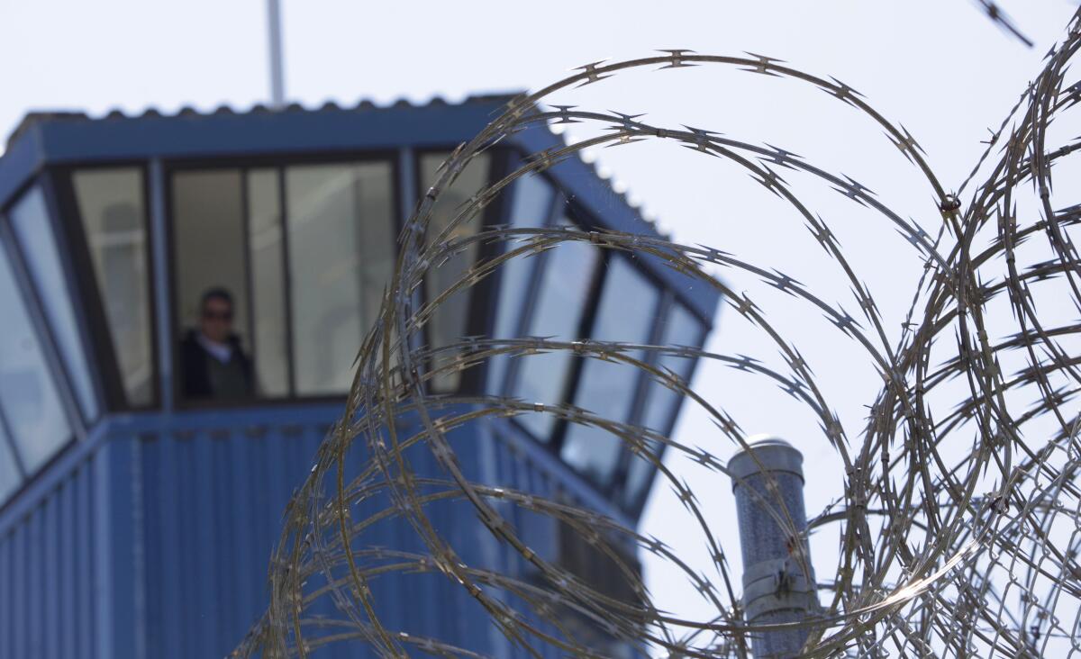 Barbed wire surrounds a prison tower with a guard inside.