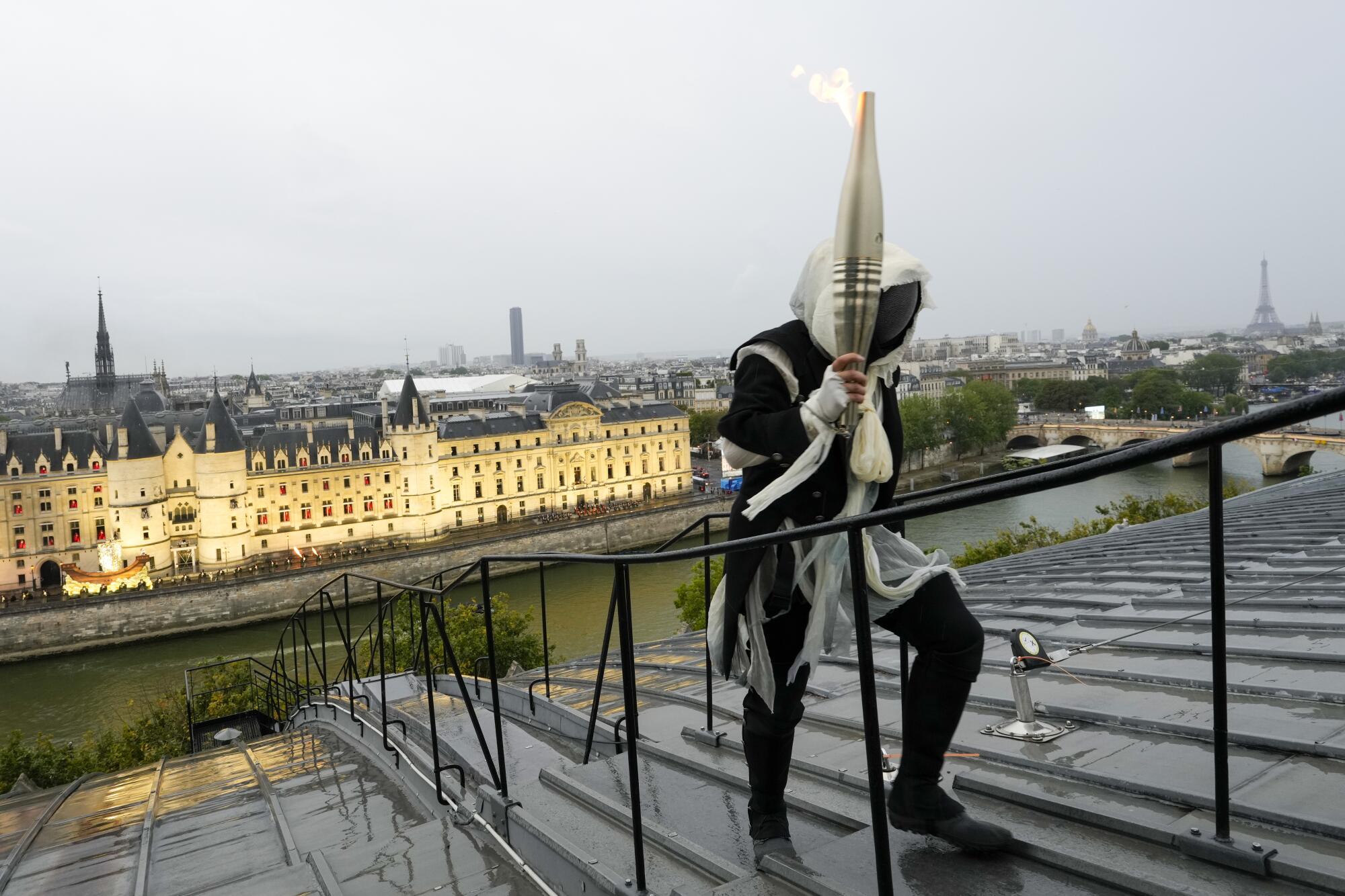 A torchbearer carries the Olympic flame over a building along the Seine River.